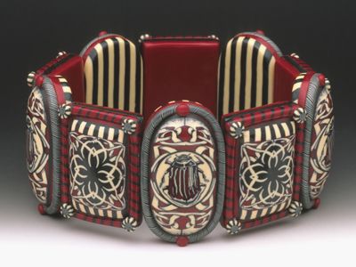 A bracelet by Sarah Shriver featuring red black and white polymer clay beads with a beetle and floral tile design.